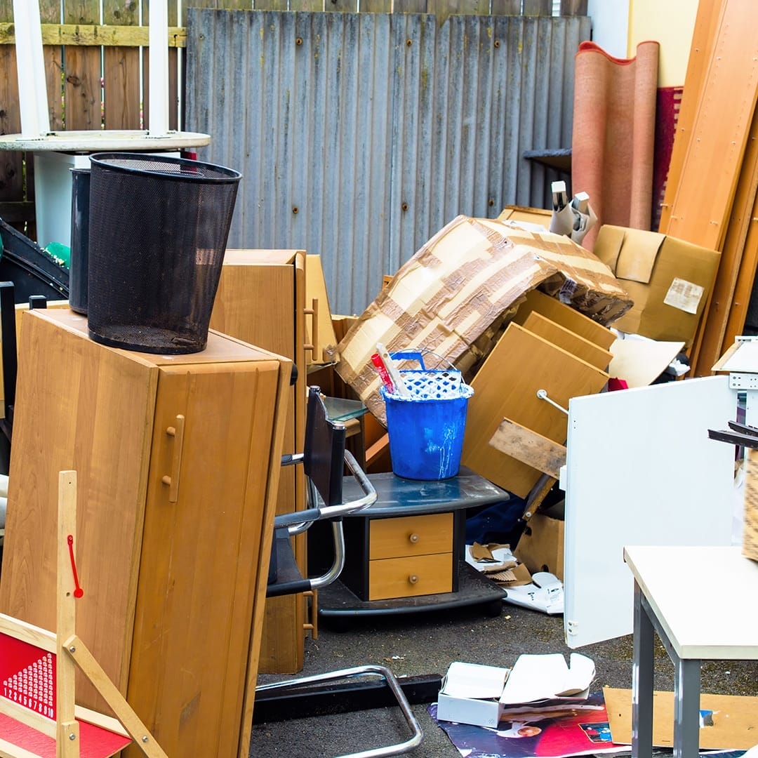 A cluttered yard area with old wooden furniture, chairs, cardboard, and bins stacked together for junk hauling services