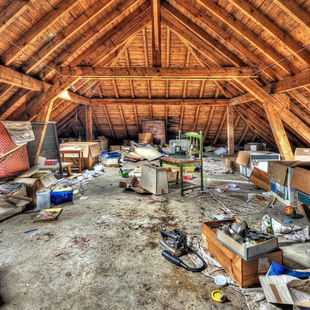 A messy attic filled with boxes, old furniture, and scattered junk, showing a space in need of professional cleanout and decluttering services