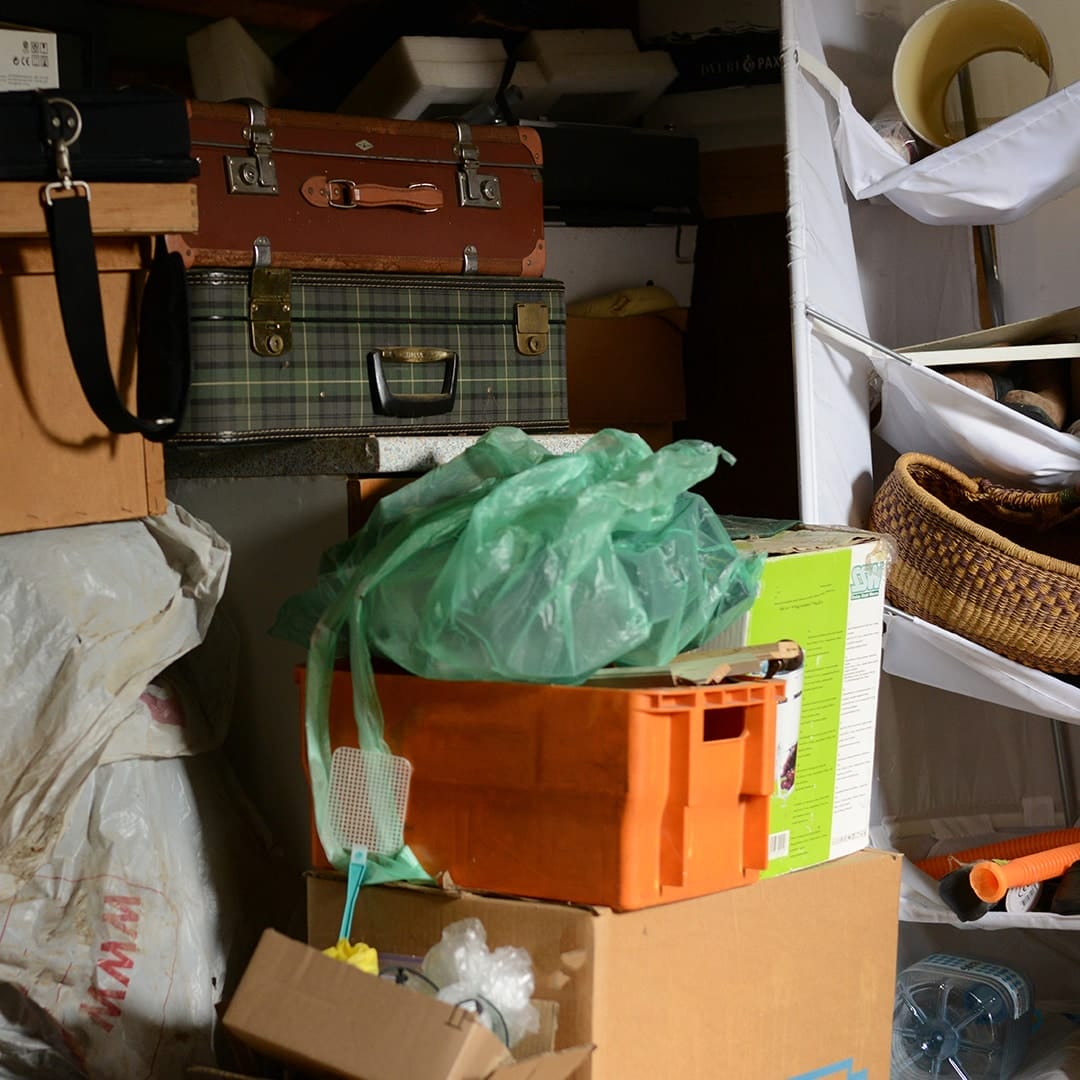 Cluttered storage area filled with boxes, bags, and miscellaneous household items, representing a garage in need of junk removal