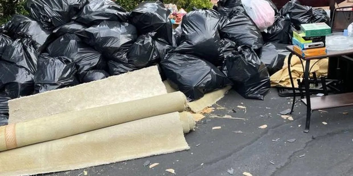 Rolled-up carpet and piles of black trash bags left outside, awaiting junk removal pickup
