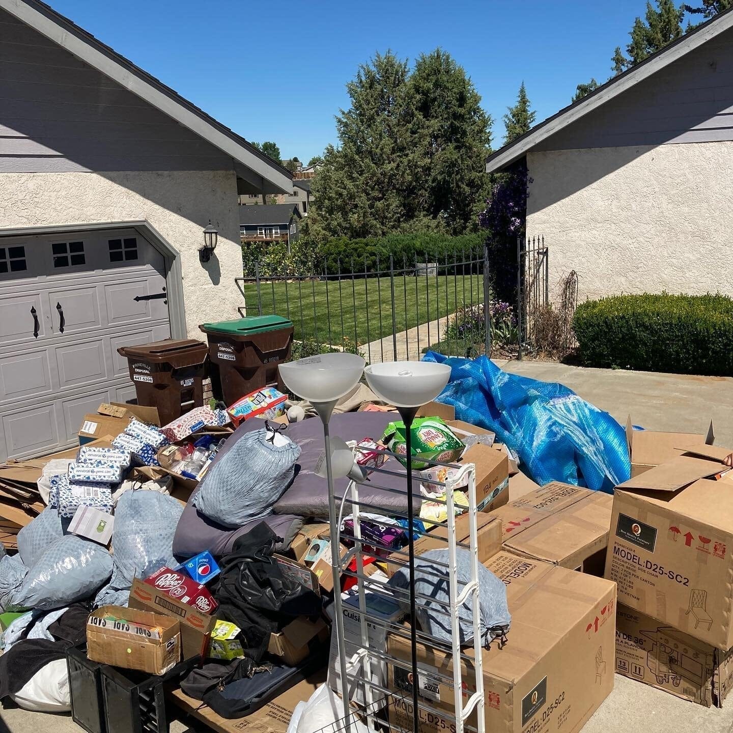 A driveway cluttered with cardboard boxes, furniture, and junk items, awaiting pickup for home cleanout services