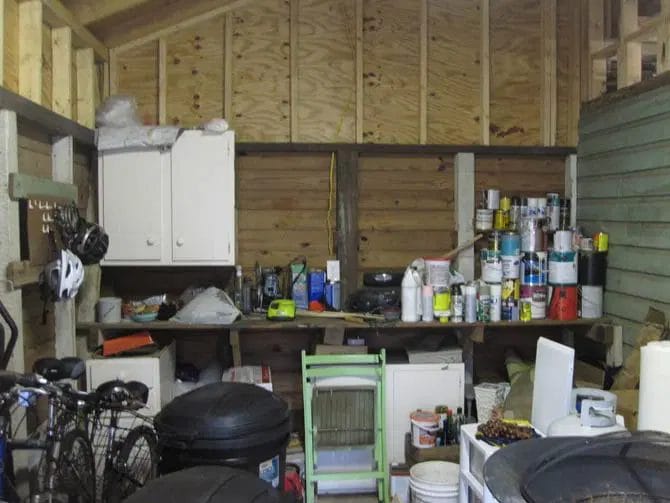 Shed interior packed with paint cans, bikes, and various stored items