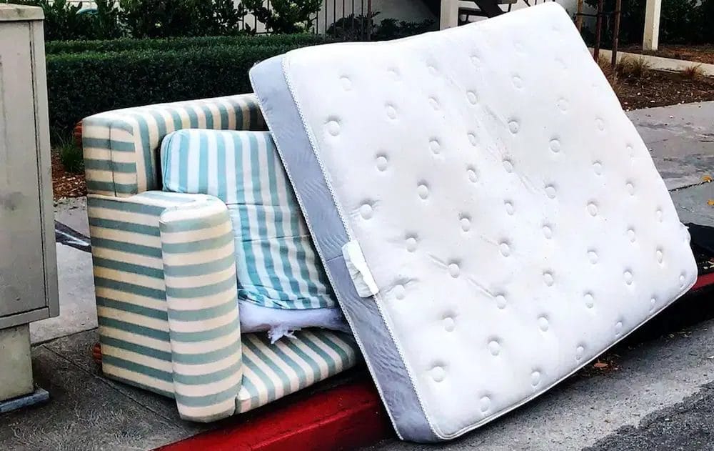 Old striped armchair and mattress left on a sidewalk for disposal