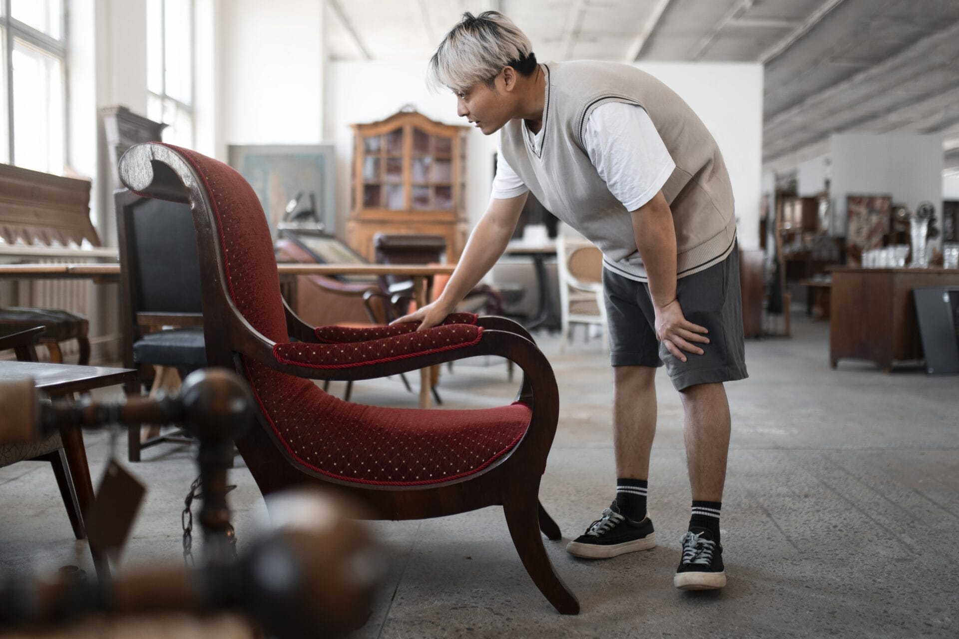 A man inspecting a vintage red upholstered chair in an antique store, representing used furniture shopping and sustainable home decor